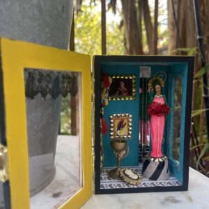 Boîte vitrine mexicaine upcyclée, porte jaune ouverte sur un intérieur turquoise avec figurine et cadres miniatures.