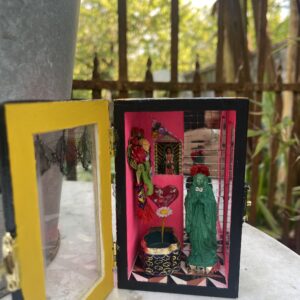 Boîte vitrine mexicaine upcyclée, porte jaune ouverte sur un intérieur rose avec figurine verte et portrait miniature de Frida Kahlo.